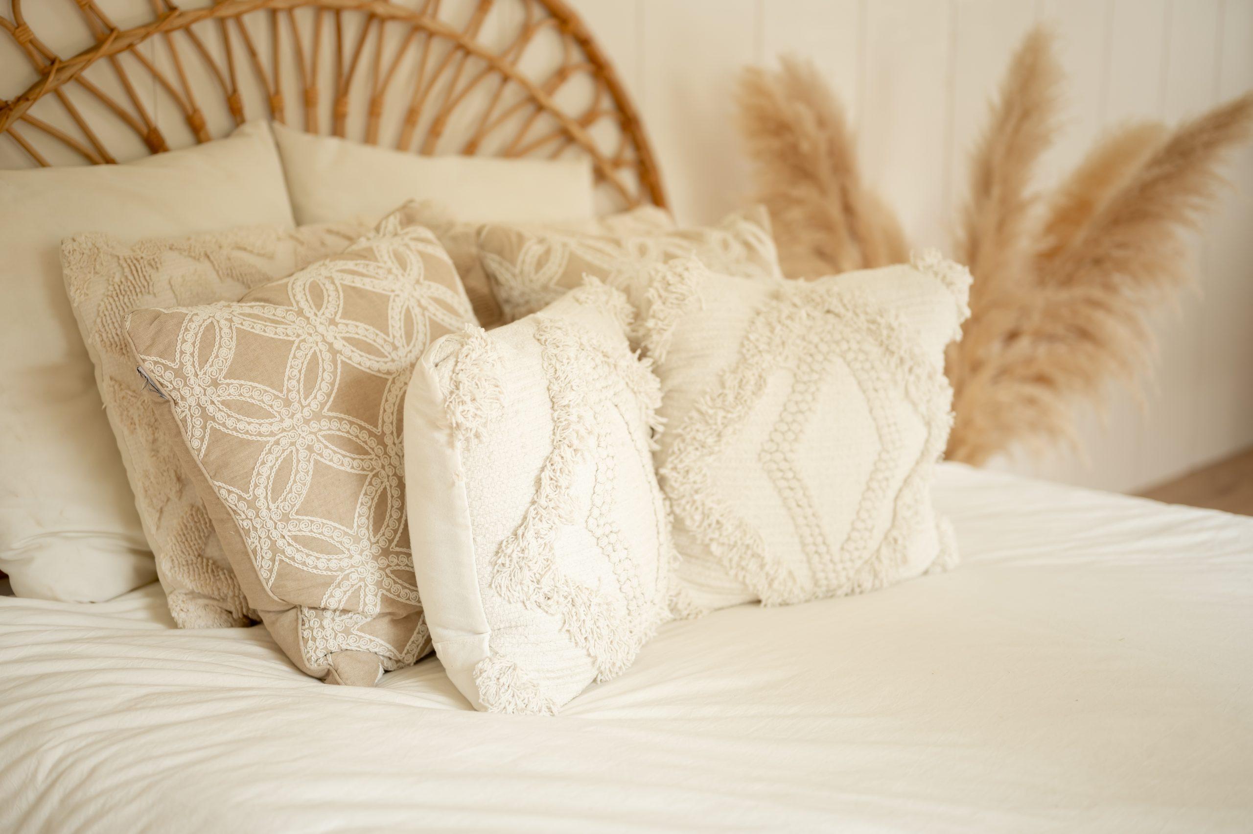 Cozy bed styled with cream and beige textured throw pillows, rattan headboard, and pampas grass decor in a boho-inspired bedroom.